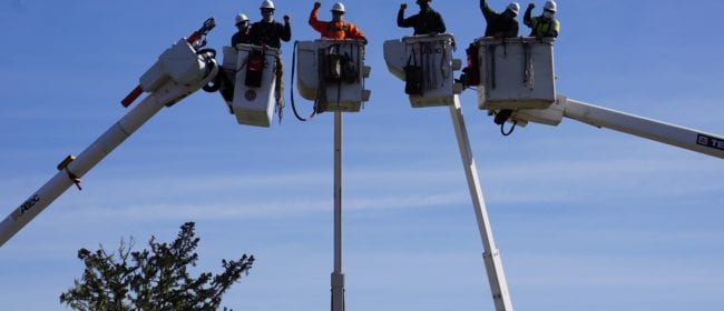 Linemen in crane buckets holding one arm in the air posing for the camera