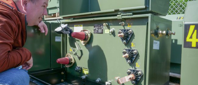 Jimmy Scarborough crouched down to look at a padmount transformer