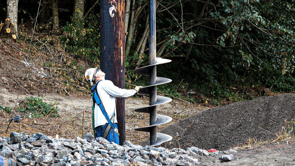 Contractor crew members used a large auger bit to bore a hole for the new pole. Here, a crew member levels the bit.