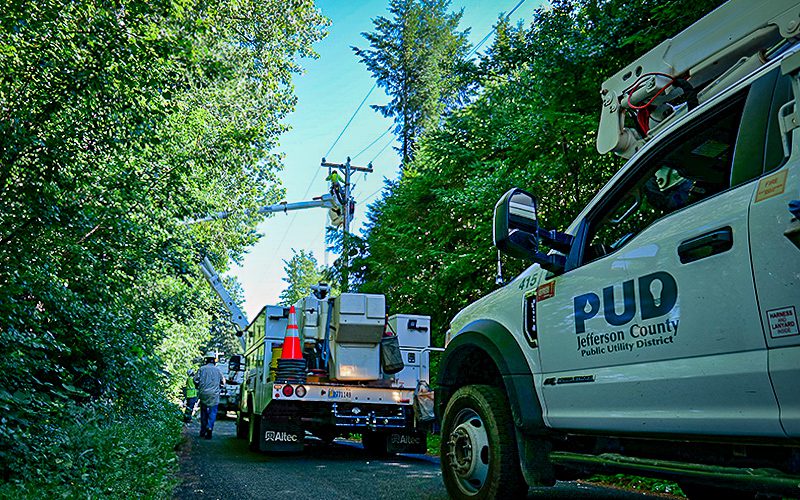 Lineman in crane bucket, PUD trucks in the foreground