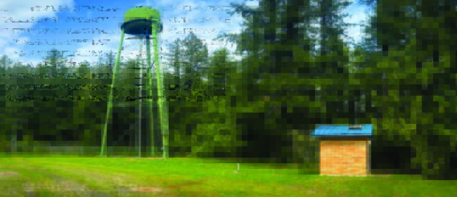 Bright lime green water tank sits in a field with a small brick shack