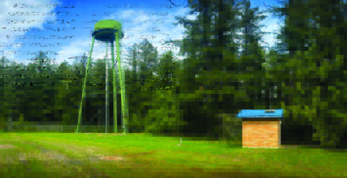 Image showing the current elevated green 30,000-gallon water tank supplying Quilcene customers. On the right side of the image is the well house that feeds the tank.