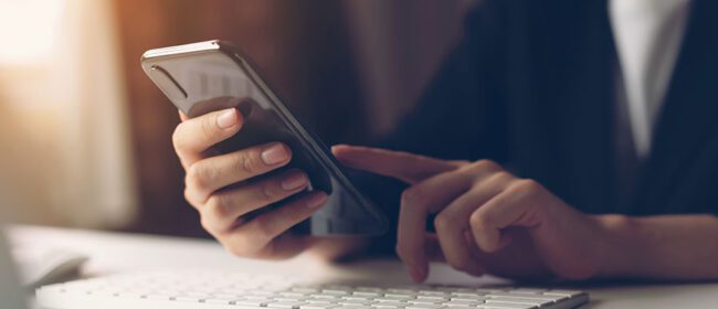image of a customer sitting at a desktop computer with a smartphone in their hand scrolling.