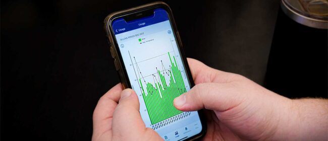 Custom hands holding a smartphone with a graph showing power usage on their Smart Hub application.