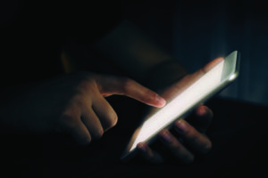 A hand holds a mobile device in the darkness. Light is cast across the hand as they check updates.