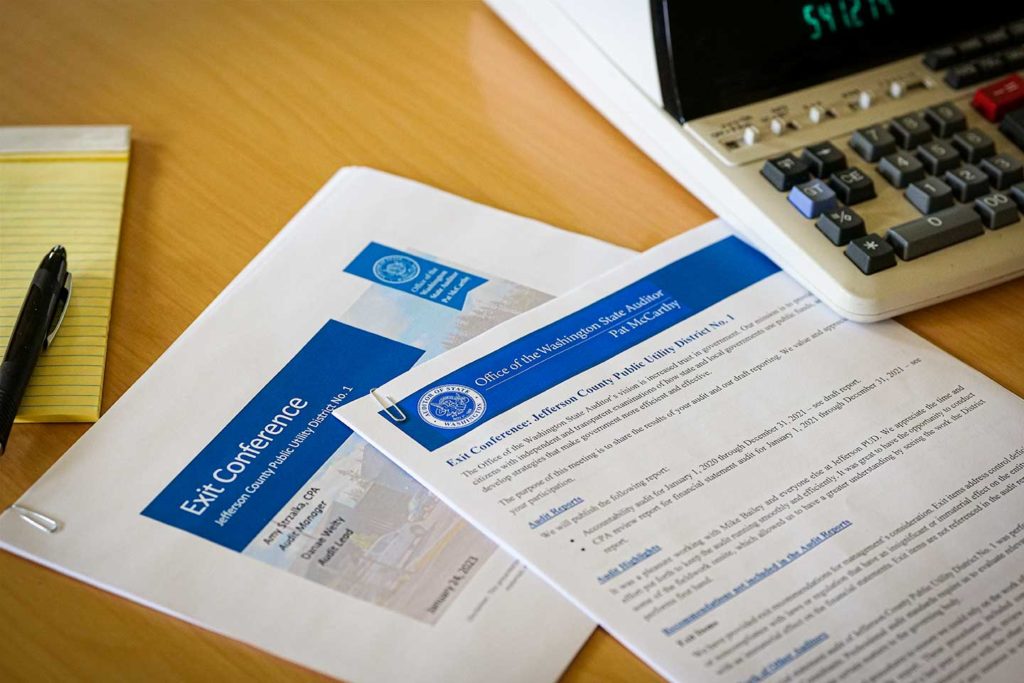 Image showing a large calculator and print outs on a conference table. Printout number one is the exit conference audio document. Print out two is the full exit conference report.