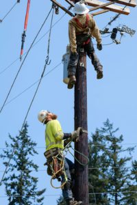 Journeyman Lineman, Dylan Brackney, climbs the utility pole to the 180-pound manikin at the top. The orange "hot stick" hangs on the left as part of the scenario.