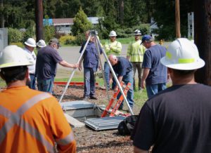 PUD Water Treatment Plant Operator, Jerry Rubert, prepares to enter the vault scene. A silver aluminum tripod with winch is positioned over the hole and is used to lift the manikin to ground level.