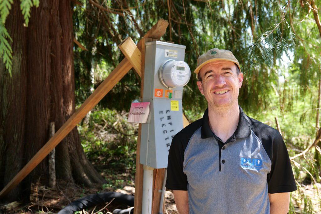 PUD Staking Engineer, Russell Miller stands beside a temporary service pole with meter visible for a new construction site.