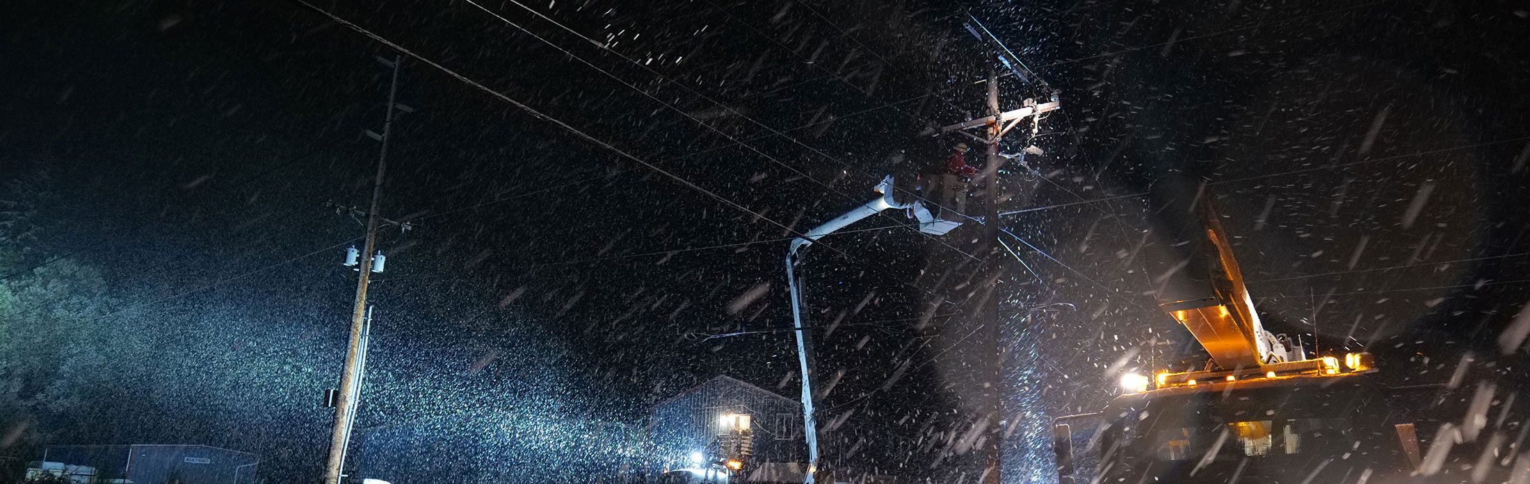 Wide view of linemen working on a utility pole in the snow on a dark night