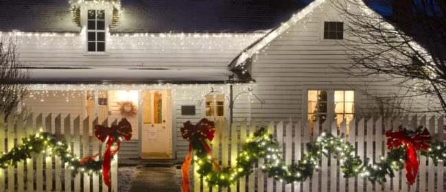 "An old ranch house, complete with white picket fence, is decked out in Christmas lights, ribbons and garlands. A Christmas tree in the window sets the scene for a romantic country Christmas.